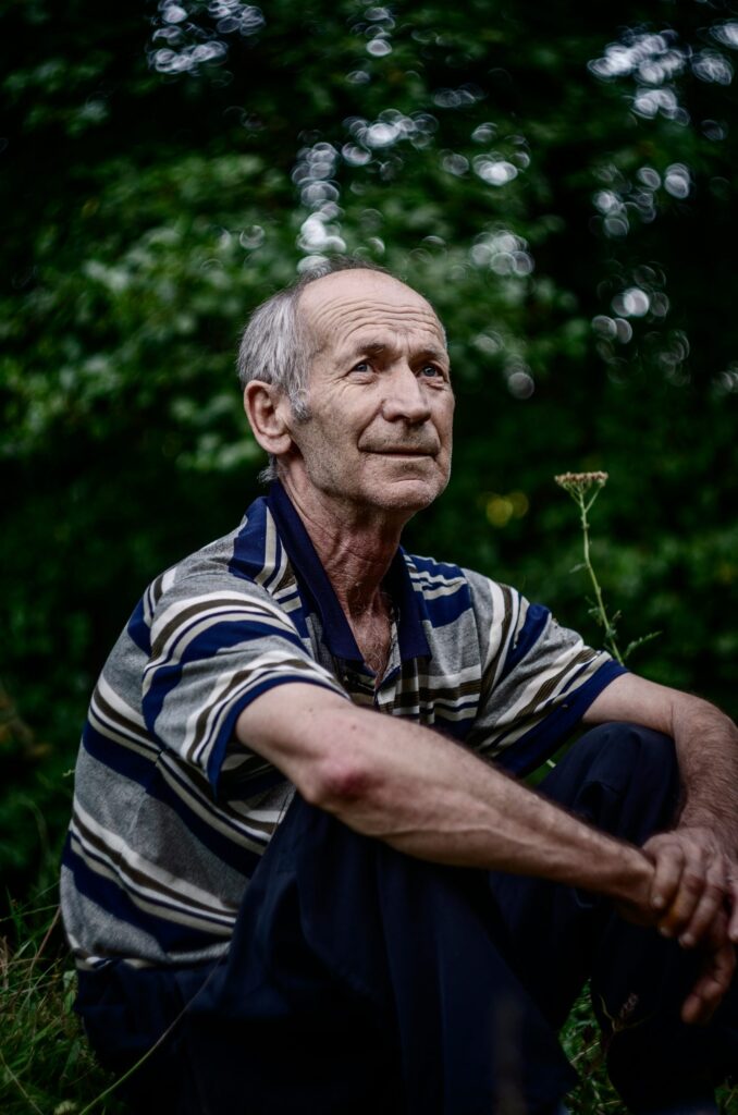 An older man sitting outdoors, thinking